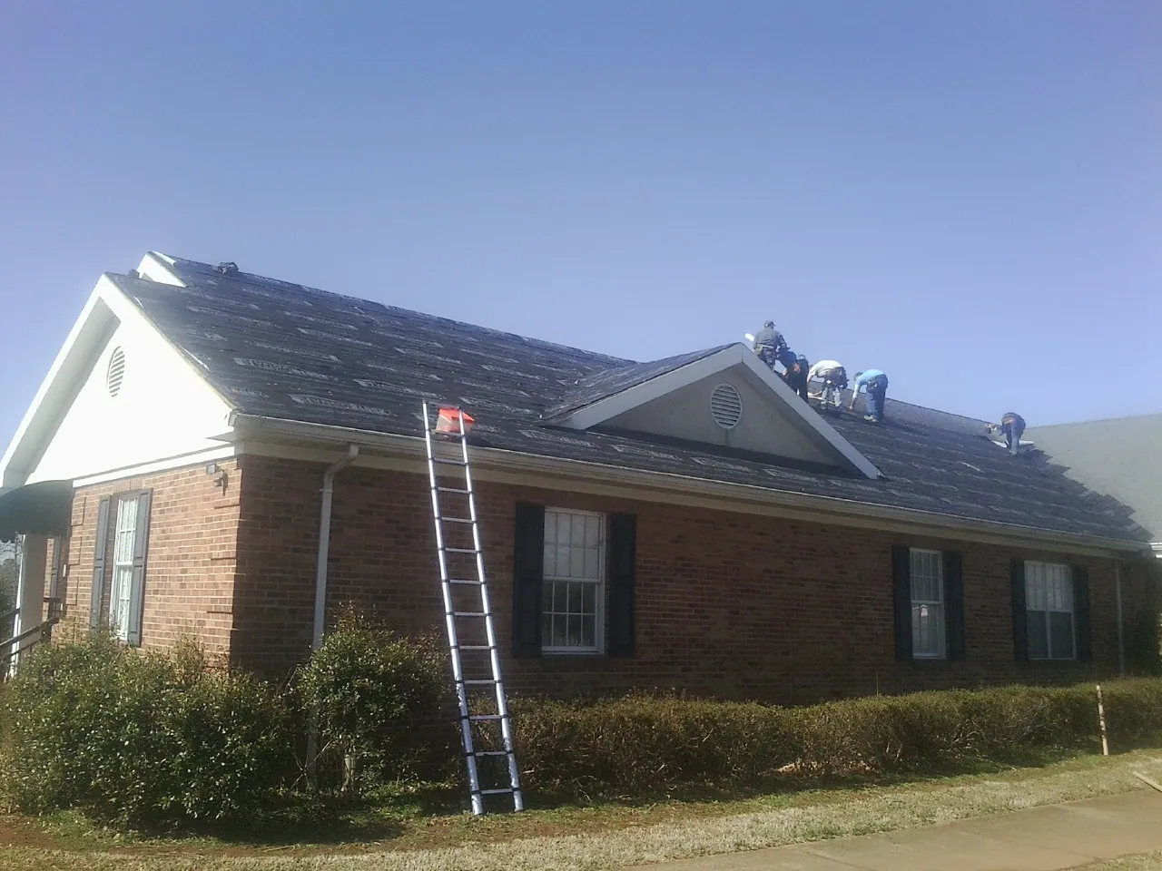 Crew tearing shingles off a brick ranch roof with a ladder set — Emergency Roof Repair work by our crew in Ponchatoula