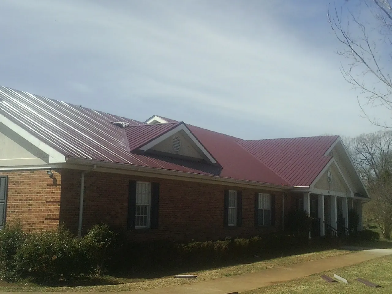 Red metal roof with gabled entries on a long brick building, from a Hail Damage Roof Repair job in Ponchatoula