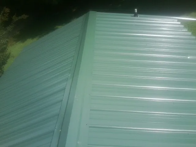New green metal panels meeting at the ridge of a roof — Flat Roof Repair work by our crew in Ponchatoula