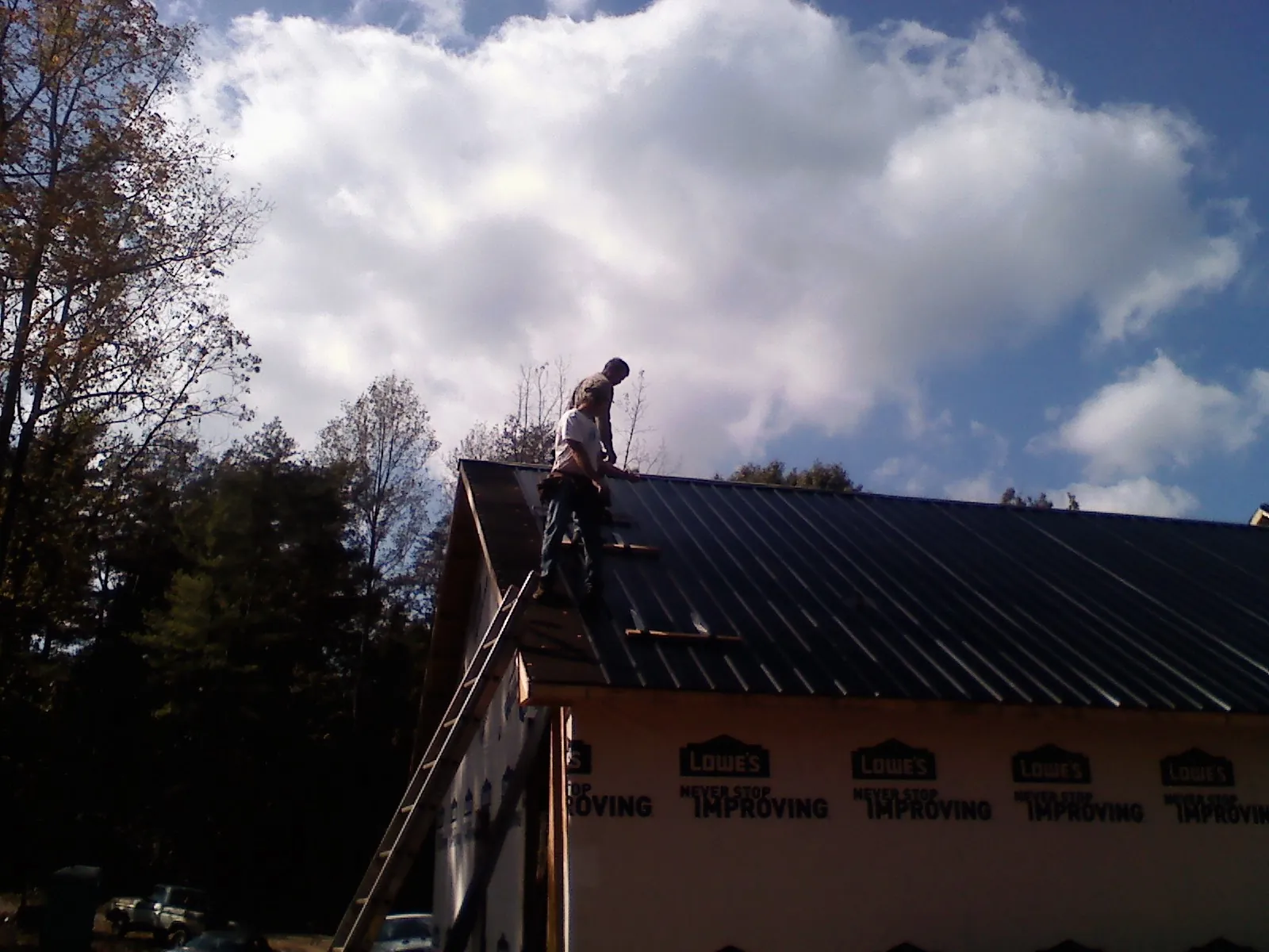 Roofer fastening dark metal panels high against a cloudy sky, from a Roof Inspection job in Ponchatoula