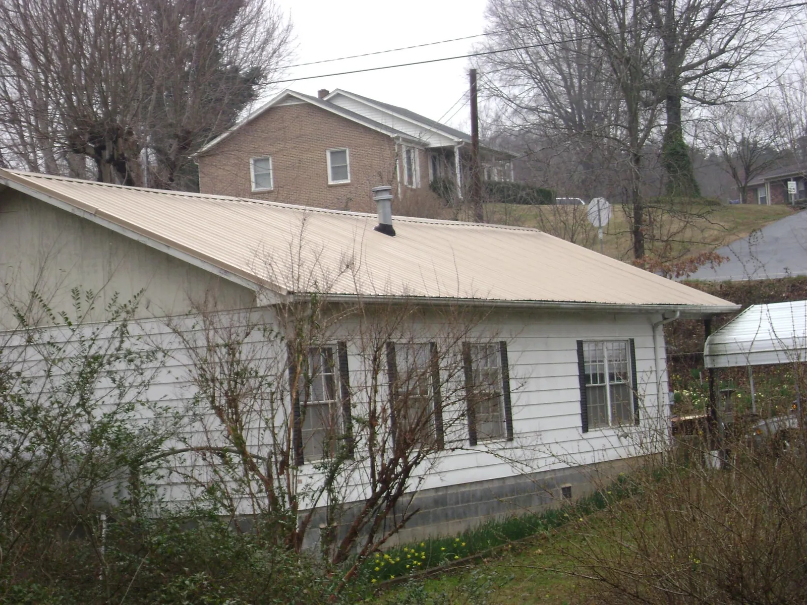 Tan metal roof on a white sided house set into a hillside — Commercial Roofing by Roofing Brothers in Ponchatoula